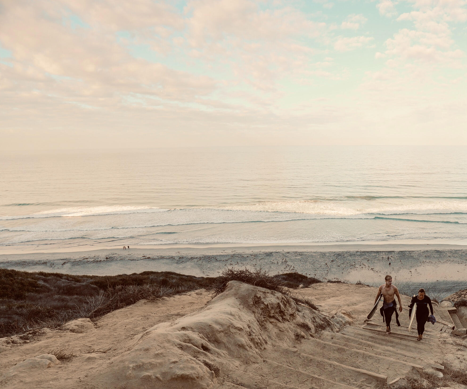 Two surfers walking upstair from the beach with boards, friendly, relaxed energy
